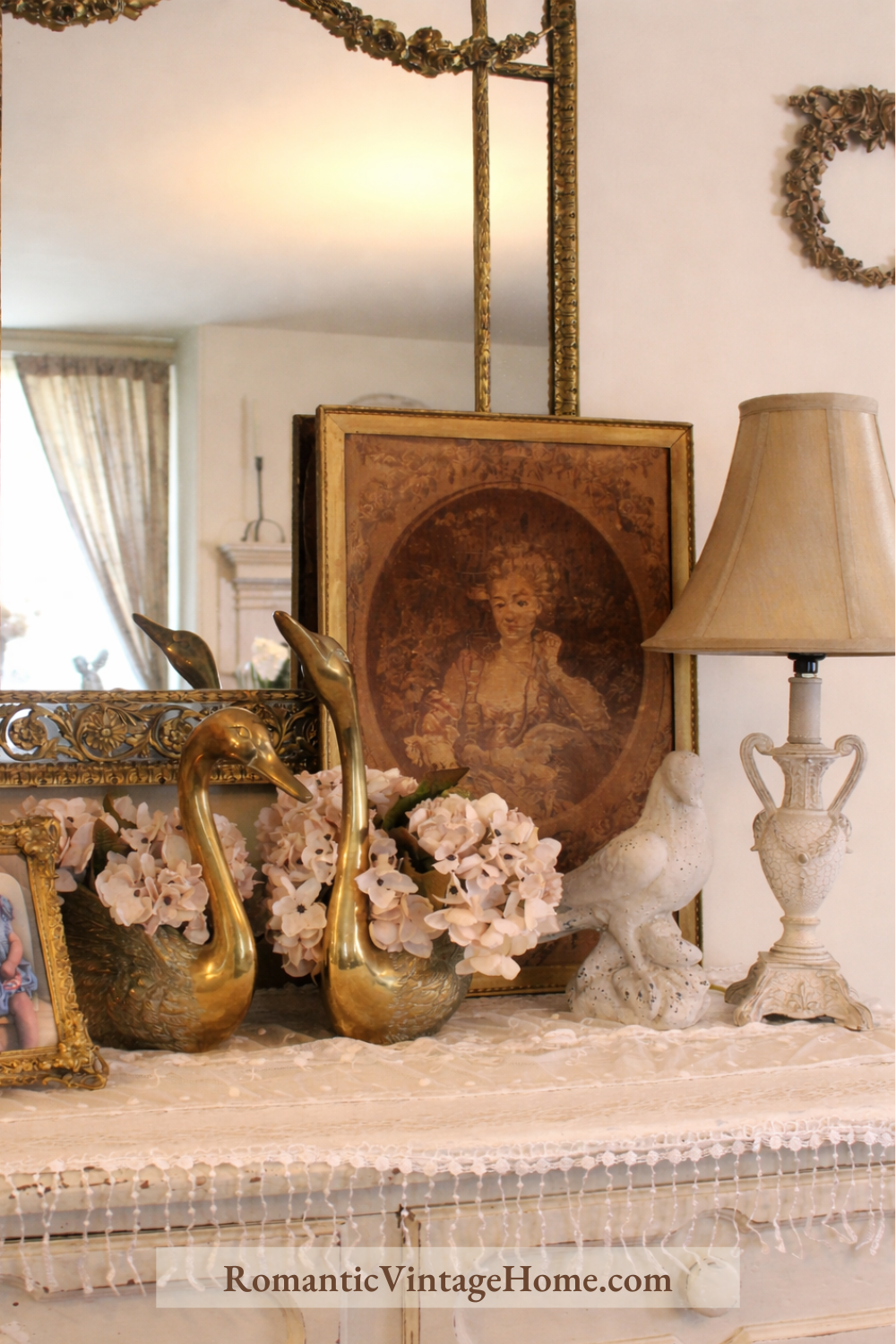 Vintage dresser vignette with an antique portrait, gold mirror, brass swan planters, and collected romantic decor